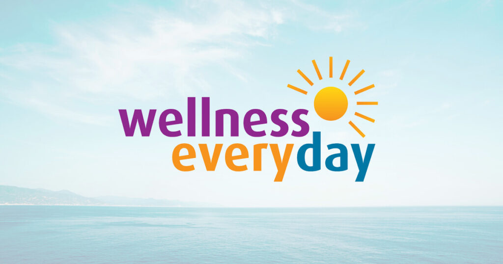 The Wellness Everyday logo. Colorful text with an animated sun over a sea and sky scape background.